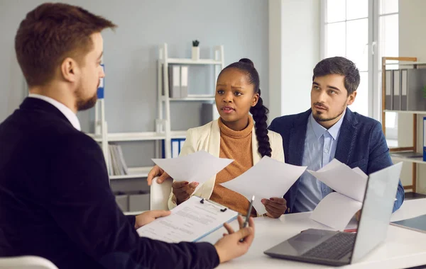 rebranding Trois professionnels en réunion, avec une femme interrogeant un homme face à elle tout en tenant des documents.