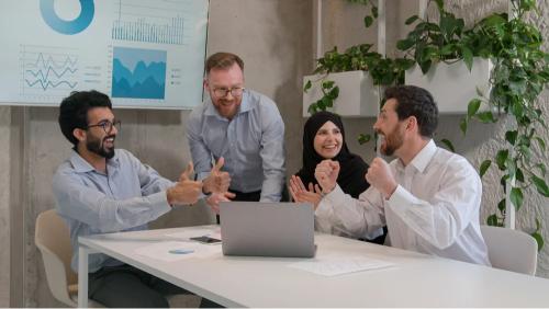 Équipe marketing multiculturelle célébrant le succès d’un projet digital autour d’un ordinateur portable, illustrant la collaboration, la performance web et la transformation digitale en entreprise.