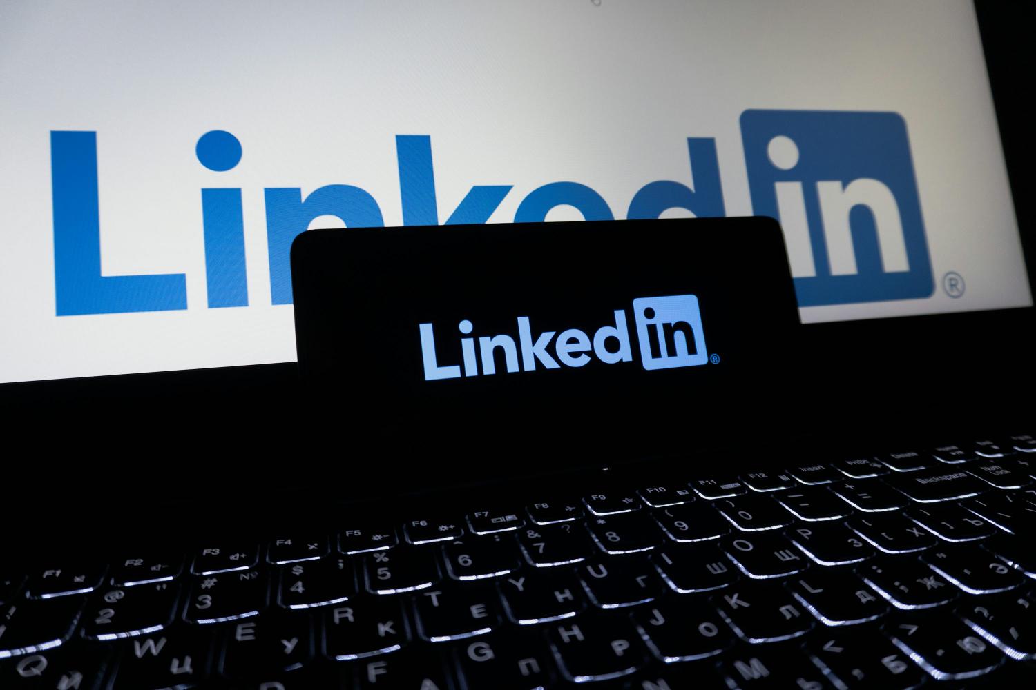 Logo LinkedIn affiché sur l’écran d’un ordinateur portable, avec un smartphone posé devant montrant également le logo LinkedIn sur fond sombre.