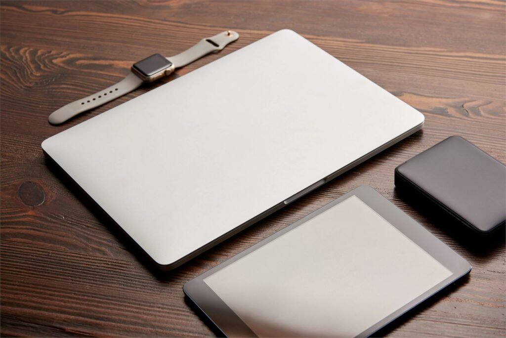 Closed laptop, tablet, smartphone and smartwatch arranged on a dark wooden desk