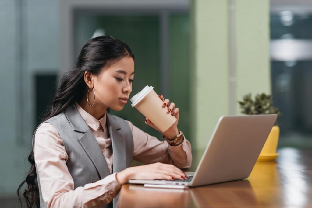Small business owner drinking coffee while working on a laptop at an office desk