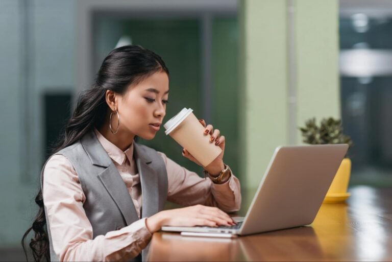 Small business owner drinking coffee while working on a laptop at an office desk